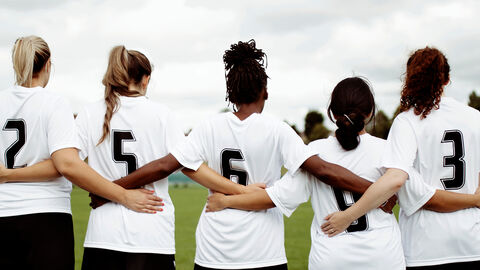 Fünf Fußballerinnen im Trikot stehen mit dem Rücken zur Kamera in einer Reihe und haben die Arme umeinander gelegt.